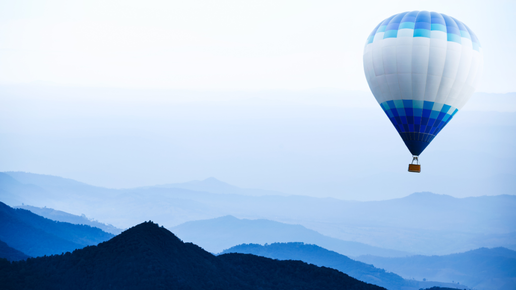 Mongolfiera che vola sopra una catena montuosa nelle prime ore del giorno